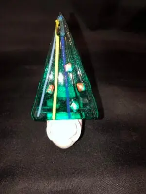 A small green glass Christmas tree Nightlight adorned with colorful embellishments stands on a white base against a dark background.