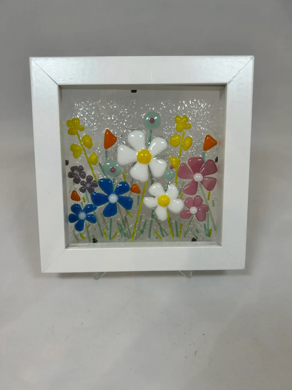 The Enchanted Garden is a framed glass art piece showcasing multicolored flowers with white, pink, and blue petals.