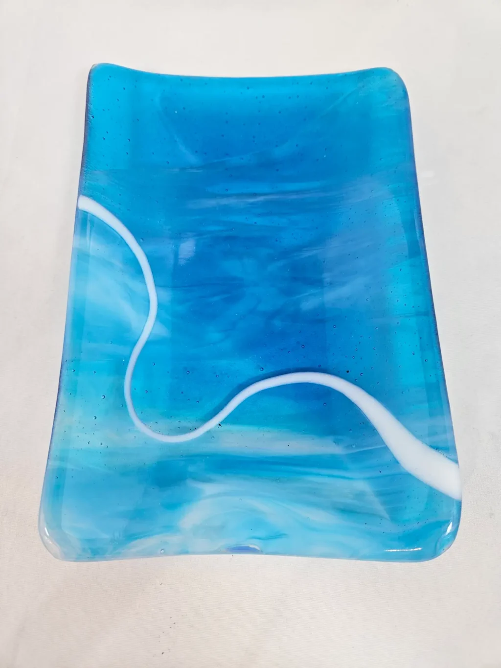 The Tranquil Drift is a rectangular, translucent blue glass tray featuring swirling white accents.