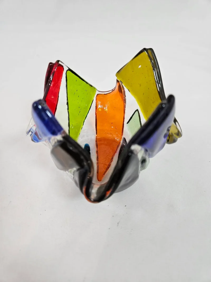 The Prism Flame is a colorful glass sculpture with an abstract, folded shape, featuring vibrant sections of red, green, orange, yellow, blue, and black.